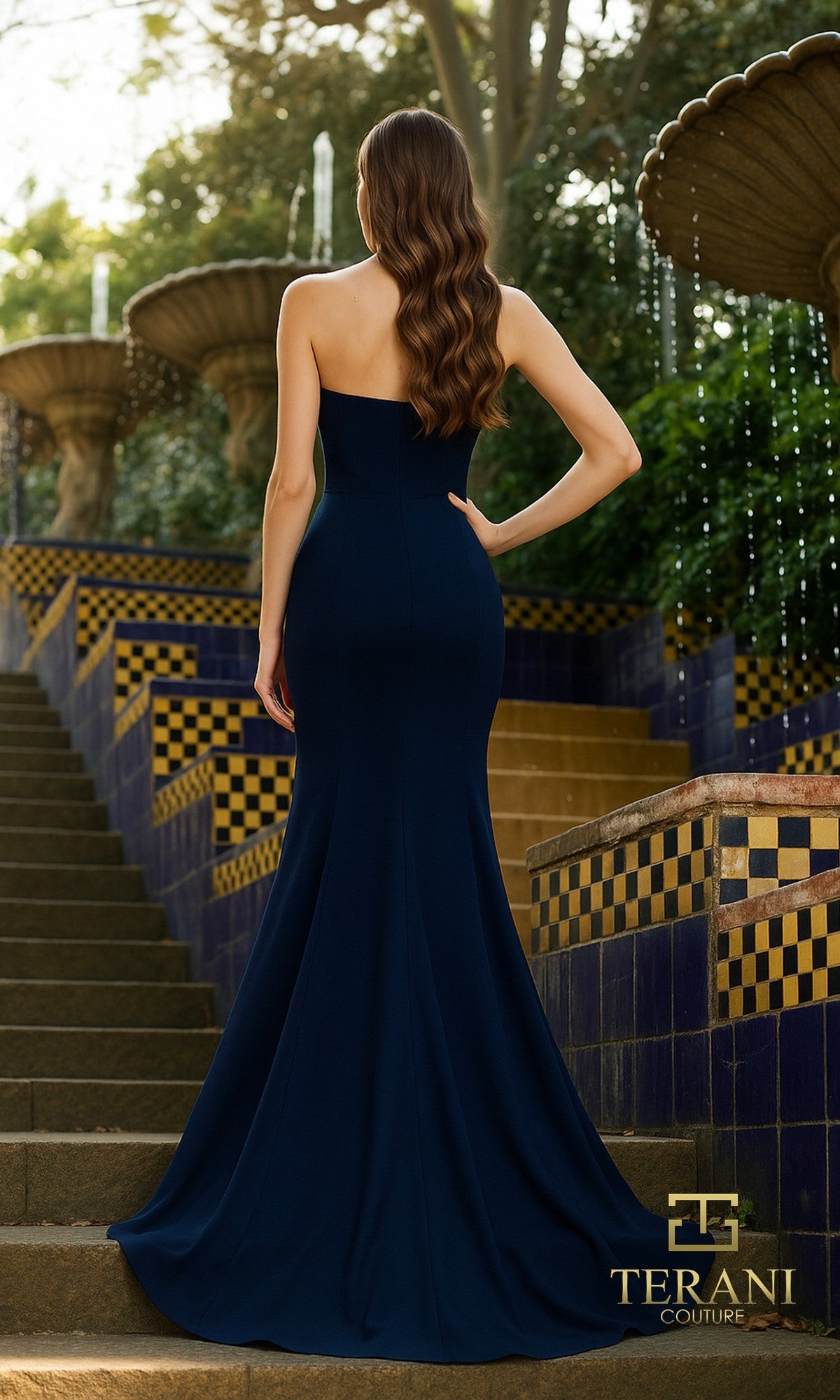 A woman in the Long Formal Dress: Terani 261P6624, a strapless Mikado gown with 3D floral appliques, stands on stone steps by tiled fountains, facing away from the camera.